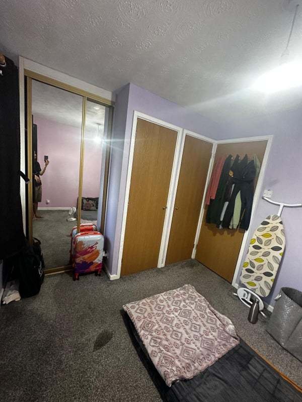 A rental ad for a £1,050/month room in Dunstable, featuring minimal furniture and a mattress on the floor, is ridiculed as "delusional." The room is for two single girls or one couple.