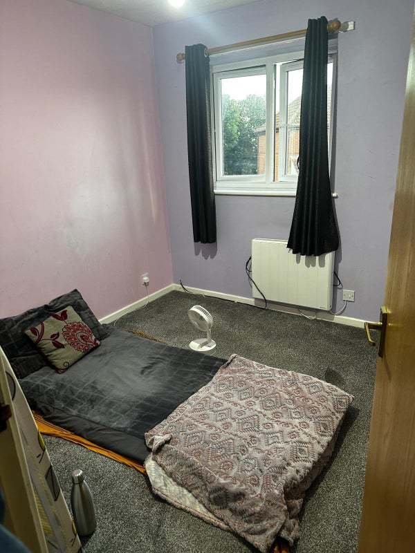 A rental ad for a £1,050/month room in Dunstable, featuring minimal furniture and a mattress on the floor, is ridiculed as "delusional." The room is for two single girls or one couple.