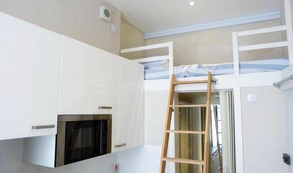 A tiny London studio flat with a bed suspended above the bathroom is up for rent at £910/month, offering limited space but proximity to amenities and transport.