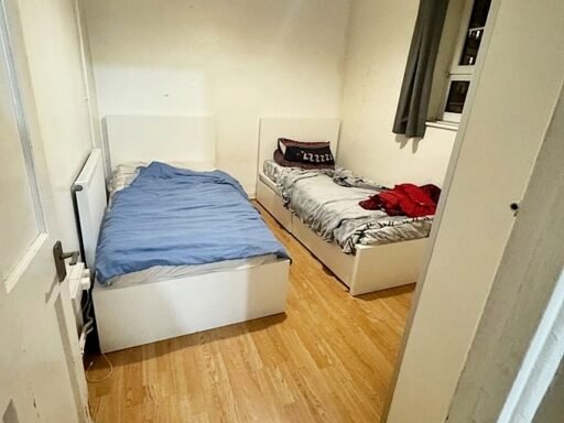 A tiny shared bedroom in Greenwich, London, is listed for £1,500 a month, offering two single beds, minimal space, and bills included, in a vibrant, well-connected location.