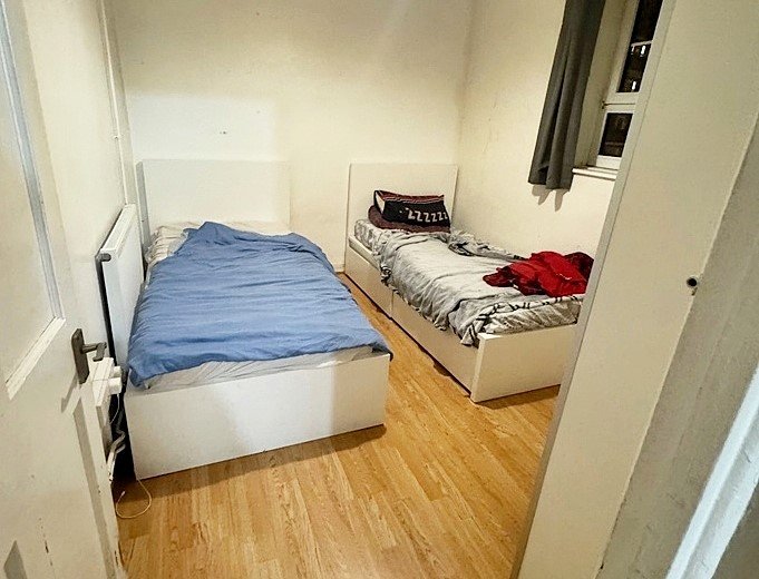 A tiny shared bedroom in Greenwich, London, is listed for £1,500 a month, offering two single beds, minimal space, and bills included, in a vibrant, well-connected location.