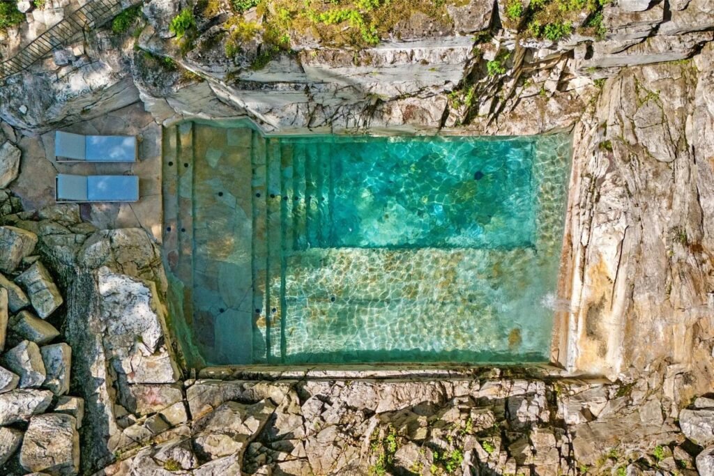 A \$3.25m Massachusetts estate features a quarry-carved pool with a 16ft waterfall, lush gardens, a canopy porch, and serene luxury across 3,459 sq ft of private grounds.