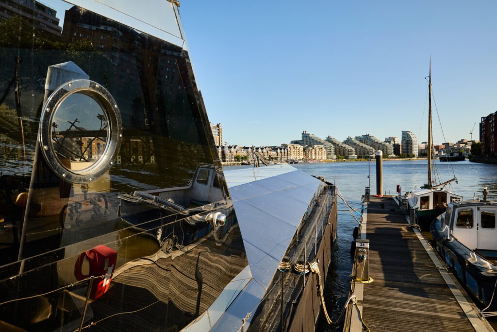A £1.15m floating sculpture moored in Fulham, Wonderland is a mirrored grain barge turned bohemian home with chandeliers, Thames views and historic artistic charm.
