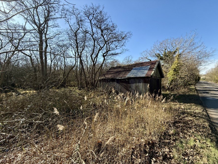A rundown former boathouse in Horning, Norfolk Broads, with peeling paint and a rusty roof, is up for sale at £25,000, offering restoration potential in a scenic location.