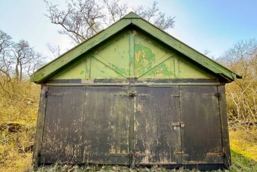 A rundown former boathouse in Horning, Norfolk Broads, with peeling paint and a rusty roof, is up for sale at £25,000, offering restoration potential in a scenic location.